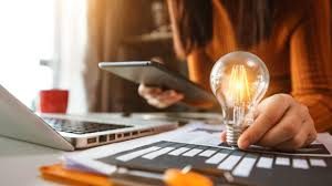 Person holding a tablet while examining a lit light bulb on a desk with papers and a laptop. One-on-one brainstorming sessions.
Feasibility 